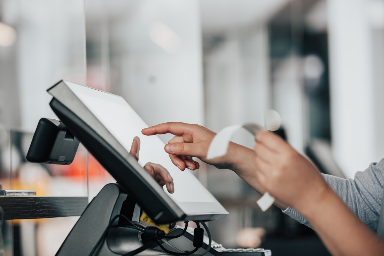 PLS case study Young saleswoman doing process payment on the touchscreen POS, counting sale in the cash register, finance concept